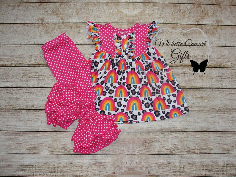Puede incluir: Un conjunto de leggings con volantes de lunares rosa y blanco con un vestido de estampado de arco&iacute;ris y leopardo. El vestido tiene cierre de bot&oacute;n y mangas con volantes.