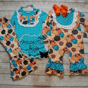 Puede incluir: Dos conjuntos de ropa infantil con tem&aacute;tica de calabaza. Uno incluye una blusa turquesa con lunares blancos, un dobladillo con volantes y pantalones a juego. El otro es un mono con un lazo naranja y un estampado de calabaza.