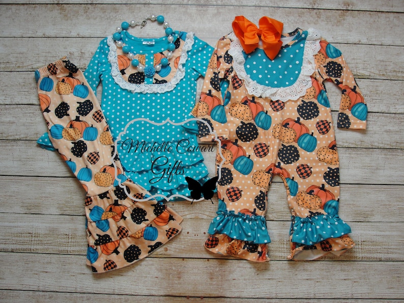 Puede incluir: Dos conjuntos de ropa infantil con tem&aacute;tica de calabaza. Uno incluye una blusa turquesa con lunares blancos, un dobladillo con volantes y pantalones a juego. El otro es un mono con un lazo naranja y un estampado de calabaza.