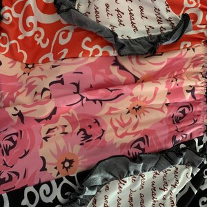 May include: A colorful fabric with floral and patterned designs. The fabric features a mix of orange, pink, and black patterns, with gray ruffled edges. Some sections include handwritten text.