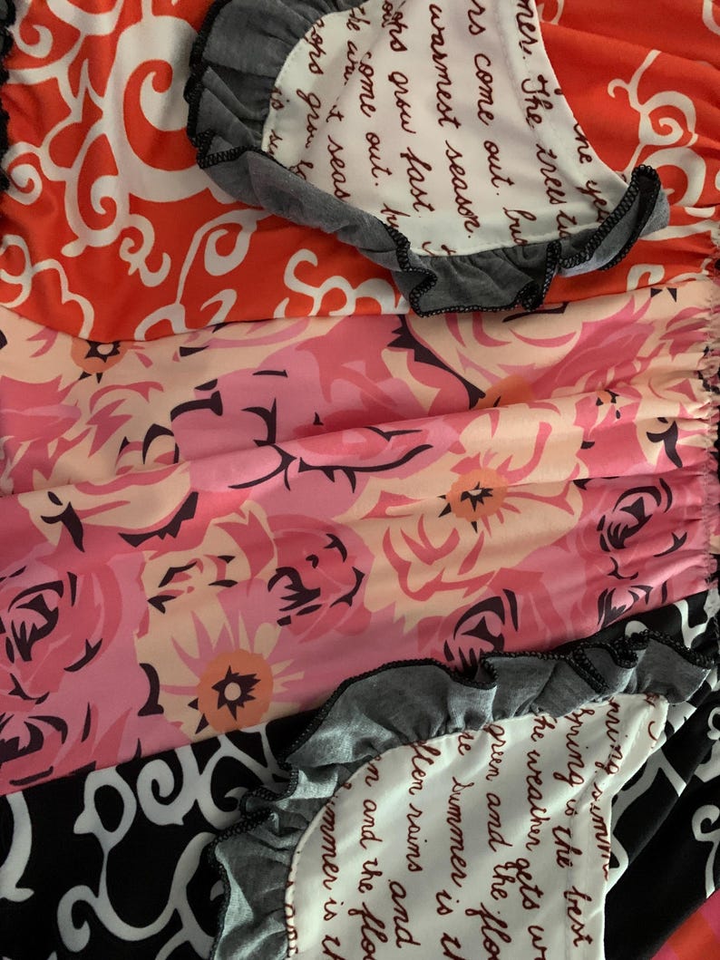 May include: A colorful fabric with floral and patterned designs. The fabric features a mix of orange, pink, and black patterns, with gray ruffled edges. Some sections include handwritten text.