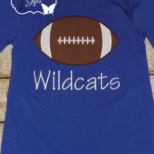 May include: A royal blue long-sleeved shirt with a brown and white embroidered football and the text "Wildcats" in white.