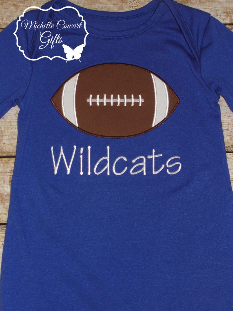 May include: A royal blue long-sleeved shirt with a brown and white embroidered football and the text "Wildcats" in white.