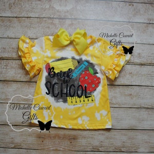 Op de afbeelding: Geel tie-dye shirt met een zwart-witte afbeelding met de tekst "Back to School" met een potlood, kleurpotlood en appel.
