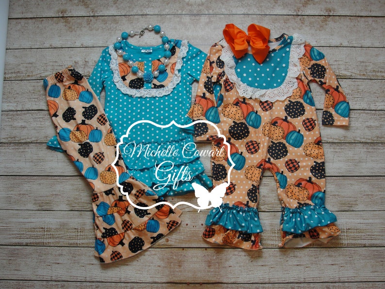 Puede incluir: Conjuntos de dos y una pieza con estampado de calabaza. Los conjuntos presentan tops turquesa y blancos con lunares, ribete de encaje y volantes. Los pantalones y el mono tienen un estampado de calabaza en naranja, negro y azul.