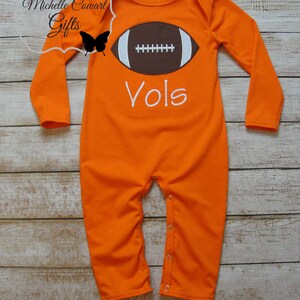 May include: Orange long-sleeve baby onesie with a brown football graphic and the word "Vols" in white embroidery.