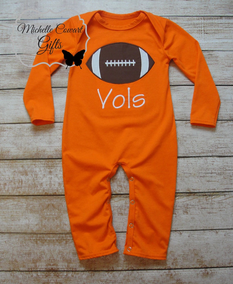 May include: Orange long-sleeve baby onesie with a brown football graphic and the word "Vols" in white embroidery.
