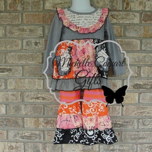 May include: A gray long-sleeved top and tiered pants set for girls. The top has a ruffled collar with floral and script details. The pants feature orange, pink, and black patterned tiers. The set is displayed on a mannequin.