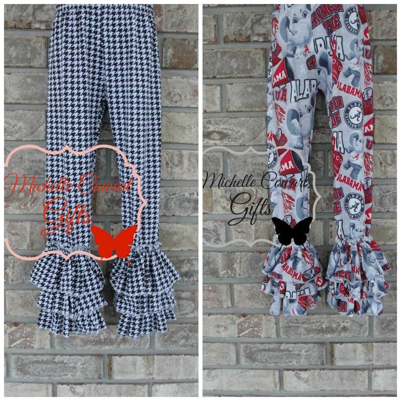 May include: Two pairs of children's pants. One pair features a black and white houndstooth pattern, and the other has a gray background with red and white Alabama-themed graphics. Both have ruffled hems.