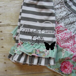 Pu&ograve; includere: Gonna a righe grigie e bianche con uno strato di pizzo verde menta con stampa floreale. La gonna ha una fascia elastica bianca. La gonna &egrave; sovrapposta a un tessuto a stampa floreale con un design rosa e bianco.