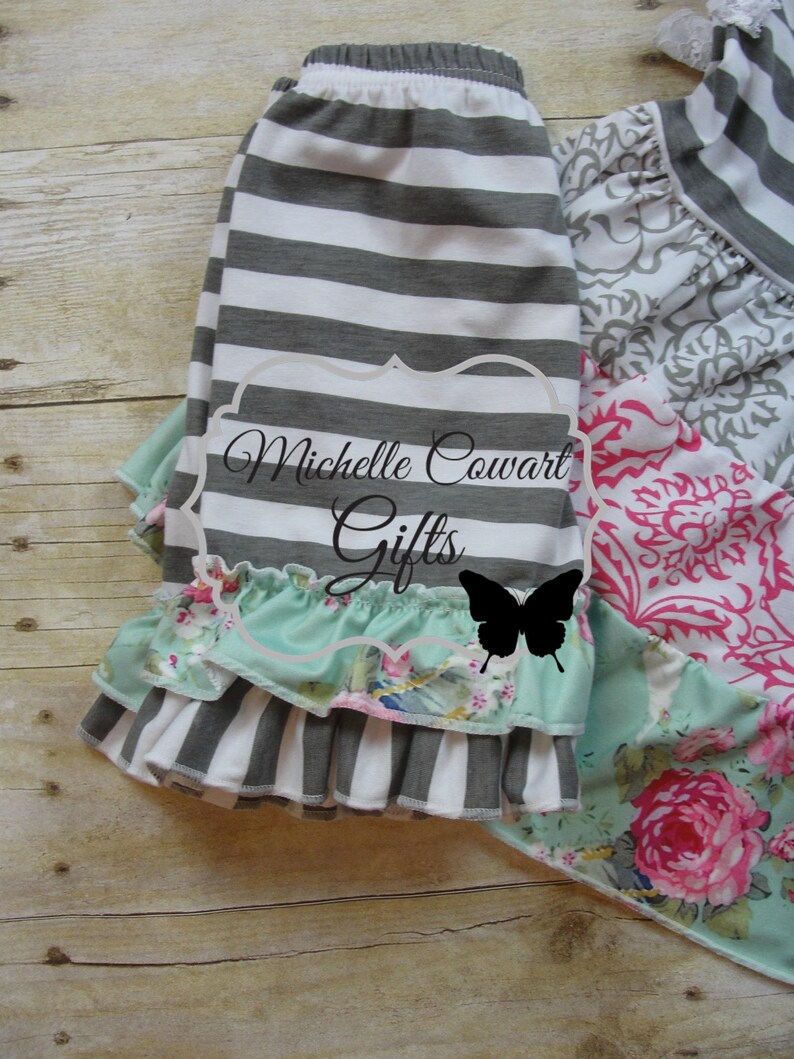 Pu&ograve; includere: Gonna a righe grigie e bianche con uno strato di pizzo verde menta con stampa floreale. La gonna ha una fascia elastica bianca. La gonna &egrave; sovrapposta a un tessuto a stampa floreale con un design rosa e bianco.