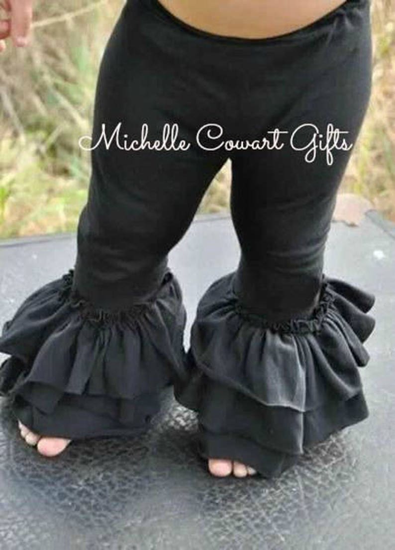 May include: Black leggings with ruffled trim at the ankles. The leggings are worn by a child. The text "Michelle Cowart Gifts" is visible on the leggings. The leggings are made of a soft material.