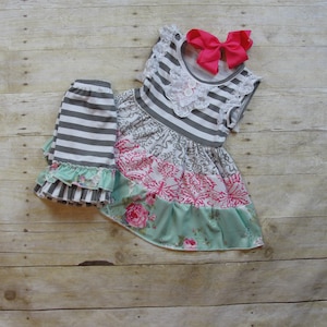Pu&ograve; includere: Una gonna a righe grigie e bianche con un bordo a balze e un vestito a stampa floreale con un corpetto a righe grigie e bianche e una gonna a stampa floreale rosa e verde. Il vestito ha un colletto di pizzo bianco e un fiocco rosa.