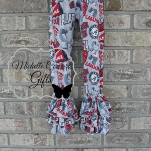 May include: Gray and red patterned leggings with ruffles at the ankles. The leggings feature the word "ALABAMA" and the Crimson Tide logo. The fabric has a repeating pattern of elephants and team-related graphics.