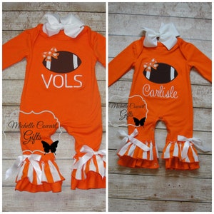May include: Two orange and white baby onesies with a football design and a white bow. One onesie says "VOLS" and the other says "Carlisle".