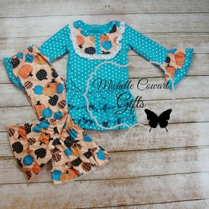 Puede incluir: Conjunto de top y pantal&oacute;n turquesa con lunares. El top tiene mangas largas con pu&ntilde;os acampanados y un dobladillo con volantes. El pantal&oacute;n presenta un estampado de calabaza. El conjunto incluye el texto "Michelle Cowart Gifts" y una silueta de mariposa.