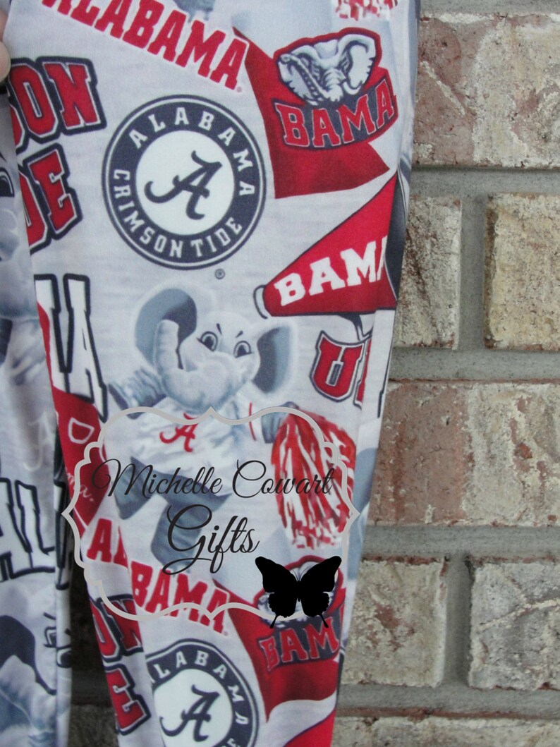 May include: Leggings with a repeating pattern of Alabama Crimson Tide logos, including the team's elephant mascot, the word "BAMA", and the "A" logo. The leggings are primarily white with red and black accents.
