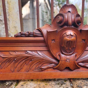 May include: A detailed, intricately carved wooden cornice with a central shield-shaped design and leafy accents. The cornice is made of rich, reddish-brown wood.