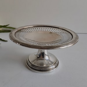 May include: A silver pedestal cake stand with a delicate, openwork design. The stand has a round base and a circular top with a raised edge.
