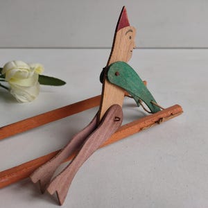 May include: A wooden toy figure of a person wearing a green and red hat, with jointed arms and legs, sitting on a wooden sled.
