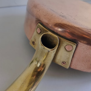 May include: A copper saucepan with a brass handle and a spout. The handle is attached to the pan with two brass rivets.