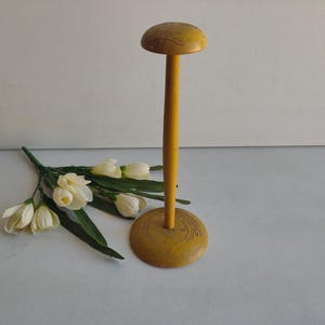 May include: A yellow wooden hat stand with a round base and a domed top. The stand is painted in a mustard yellow color. A bouquet of white flowers with green leaves is next to the stand.