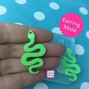 Puede incluir: Un molde de pendientes en forma de serpiente verde neón y un pendiente terminado. El molde es transparente y tiene las palabras "Earring Mold" en una estrella rosa. El pendiente terminado es de color verde brillante.