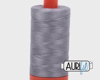 Könnte beinhalten: Eine Spule graues Garn mit einem orangefarbenen Deckel und Boden. Das Garn ist eng um die Spule gewickelt. Der Markenname "AURIfil" ist auf der Seite aufgedruckt.