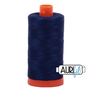 Peut inclure: Une bobine de fil bleu marine avec un dessus et une base orange. Le fil est enroulé serré autour d'un noyau cylindrique. La marque "AURIfil" est imprimée sur le côté de la bobine en lettres blanches.