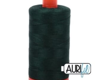 Könnte beinhalten: Eine Spule dunkelgrünes Garn mit orangefarbenem Deckel und Boden. Das Garn ist eng gewickelt, und die Spule trägt den Markennamen "AURIfil". Dieses Garn wird zum Nähen, Quilten oder für andere Textilhandwerke verwendet.