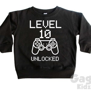 May include: Black long-sleeve sweatshirt with white text that reads "LEVEL 10 UNLOCKED" and a pixelated video game controller graphic.