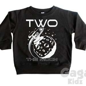 May include: Black long-sleeved sweatshirt with a white graphic of a rocket ship flying around the moon. The text "TWO THE MOON" is printed on the shirt.