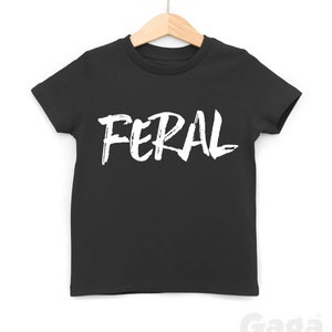 Op de afbeelding: Zwart T-shirt met witte tekst die "FERAL" zegt in een vetgedrukt, penseelstreep-lettertype.