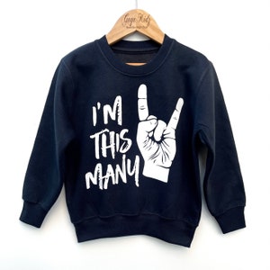 May include: A navy blue sweatshirt with white text that reads "I'm this many" and a white hand making the rock and roll hand gesture.