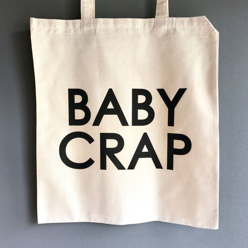 Pode incluir: Uma bolsa de lona branca com texto preto que diz "BABY CRAP".