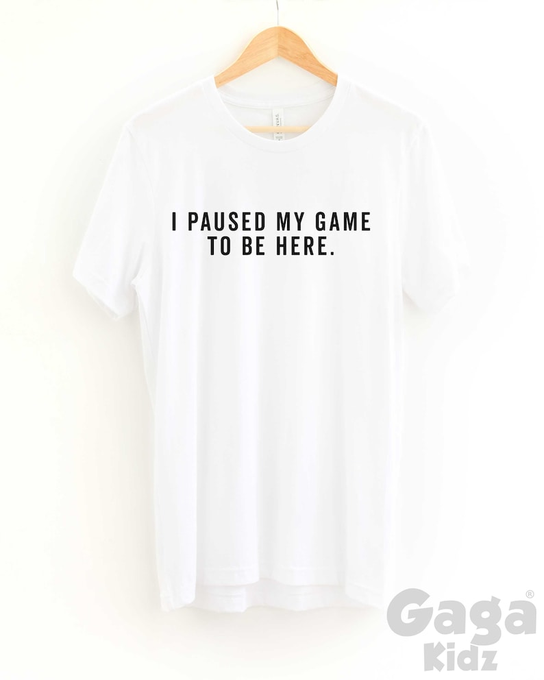 K&ouml;nnte beinhalten: Wei&szlig;es T-Shirt mit schwarzem Text, der "Ich habe mein Spiel pausiert, um hier zu sein." lautet.