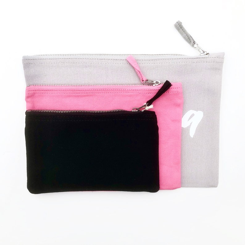 May include: Three zippered pouches in different sizes. The largest pouch is gray, the middle pouch is pink, and the smallest pouch is black.