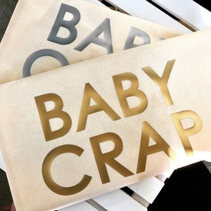 Pode incluir: Duas sacolas de lona com as palavras "BABY CRAP" impressas em letras douradas e prateadas.