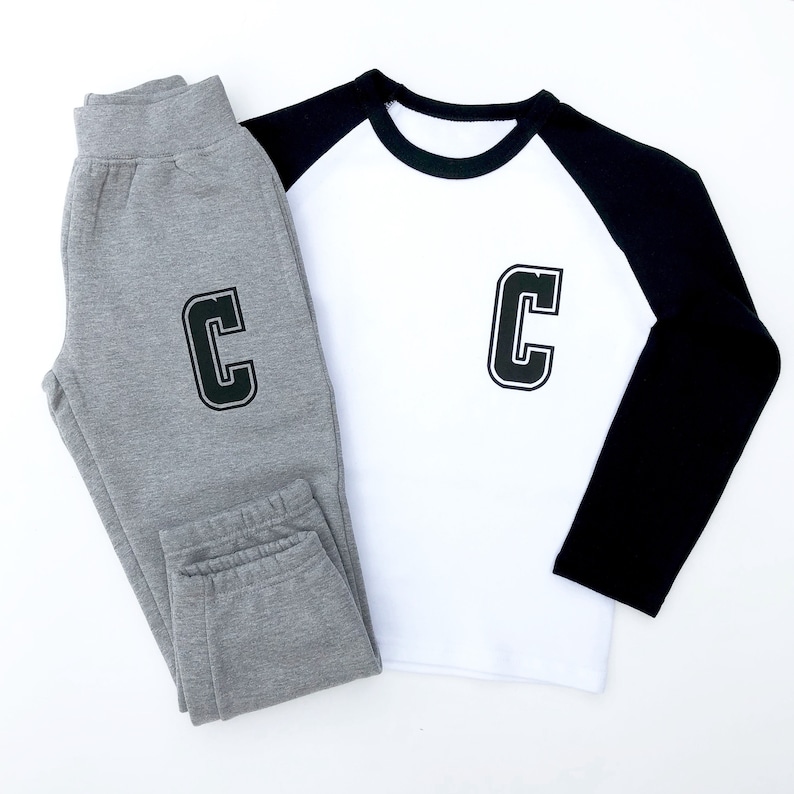 May include: A pair of grey sweatpants and a white long-sleeved top with black sleeves. Both items of clothing feature a large black letter "C" on the front.