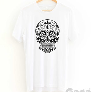 May include: White t-shirt with a black and white sugar skull graphic. The skull is decorated with floral patterns and has a diamond in the center of the forehead.