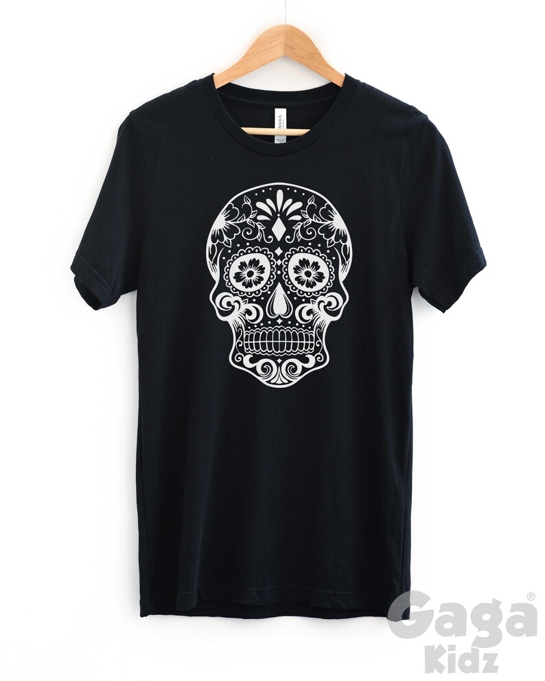 May include: Black t-shirt with a white sugar skull design. The skull is decorated with intricate floral patterns.