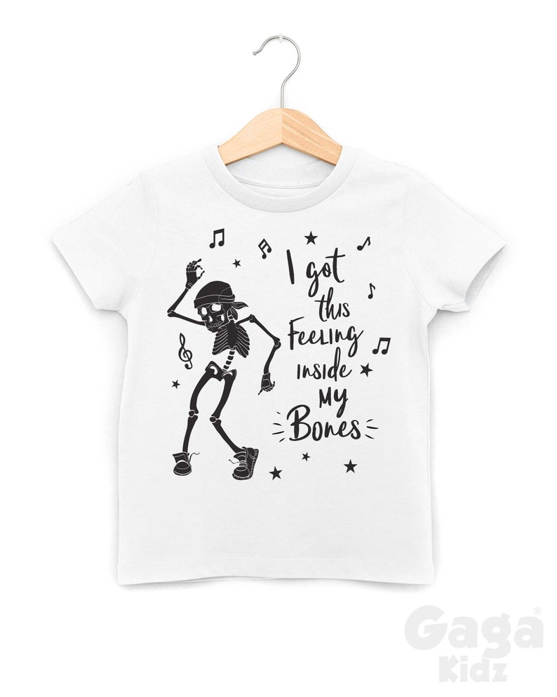 Peut inclure: T-shirt blanc avec un squelette noir dansant et le texte "I got this feeling inside my bones" avec des notes de musique et des &eacute;toiles.