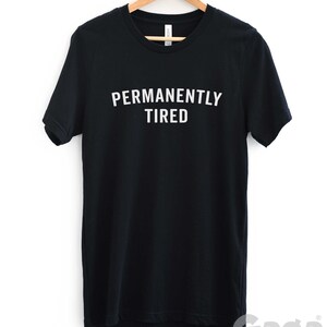 Puede incluir: Camiseta negra con texto blanco que dice "PERMANENTLY TIRED".