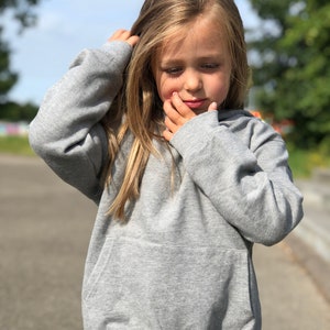 May include: A heather gray long-sleeve hooded sweatshirt featuring a front kangaroo pocket, ribbed cuffs, and a ribbed hem. The garment is constructed from a soft, knit fabric with a consistent gray tone throughout the entire piece.