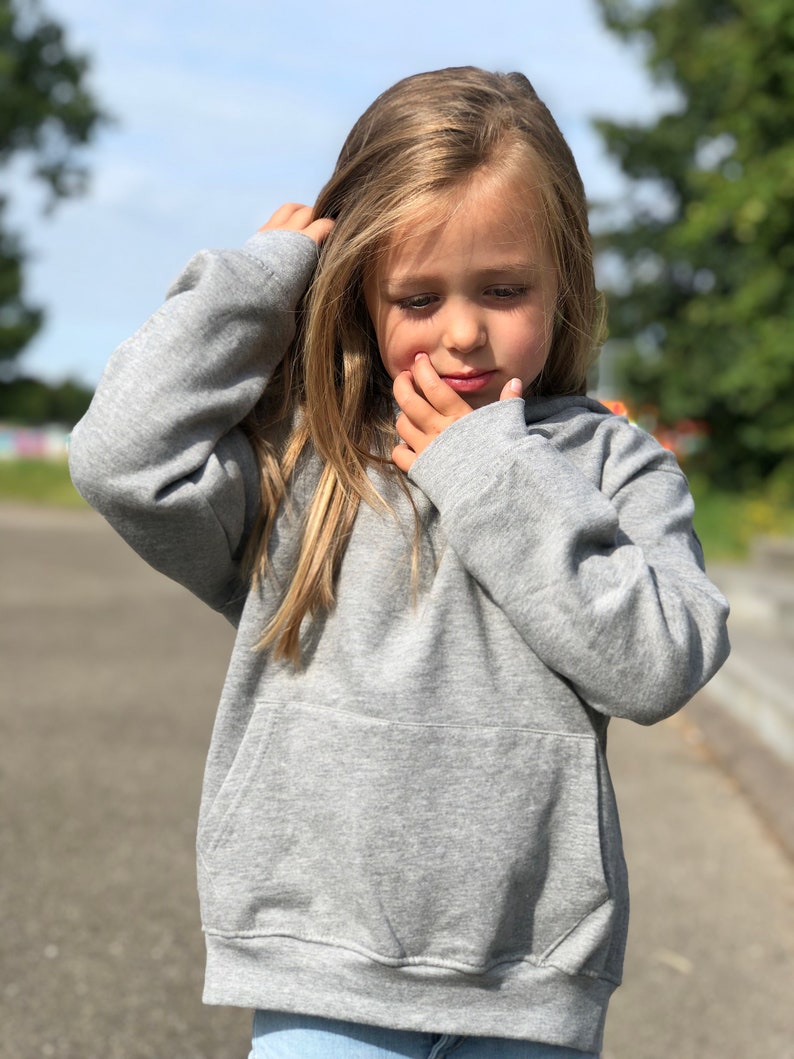 May include: A heather gray long-sleeve hooded sweatshirt featuring a front kangaroo pocket, ribbed cuffs, and a ribbed hem. The garment is constructed from a soft, knit fabric with a consistent gray tone throughout the entire piece.