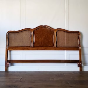 May include: A vintage-style wooden headboard with a curved top. The headboard features a central panel of burl wood, flanked by woven cane panels. The frame is a warm brown color, and the headboard is designed to fit a standard bed frame.