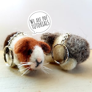 May include: Two felt animal keychains, one brown and white and one white and brown, with silver key rings. The keychains are shaped like guinea pigs. The text "We are PDF Tutorials" is in a speech bubble above the keychains.