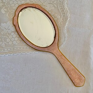 May include: A vintage hand mirror with a pink and white marbled plastic handle and a round, clear glass mirror.
