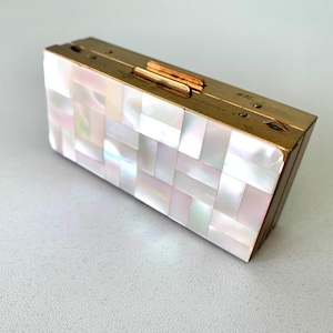 Puede incluir: Una caja rectangular de color dorado con una tapa con bisagras. La caja está cubierta con un mosaico de azulejos de nácar iridiscente.