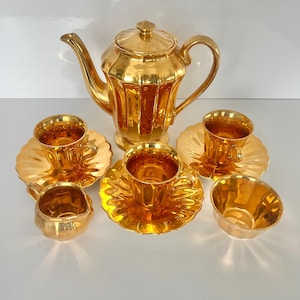 Puede incluir: Un juego de té dorado completo, que incluye una tetera con tapa, cuatro tazas con platillos y una crema. El juego tiene una superficie reflectante y brillante. Las tazas y los platillos tienen un diseño de borde festoneado.